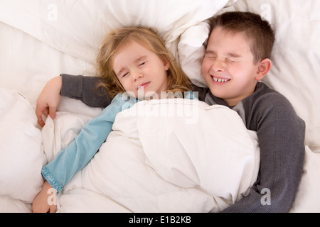 Zwei süße kleine Kinder miteinander schlafen teilen das gleiche Bett mit einem kleinen Jungen schützend, seine jüngere Schwester kuscheln Stockfoto