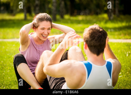 Sport-paar Sit-ups gemeinsam in der Natur auf dem grünen Rasen zu machen Stockfoto