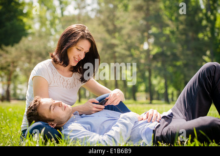 Junger Mann ist entspannend auf Frau Knien, während sie mit Smartphone spielt Stockfoto
