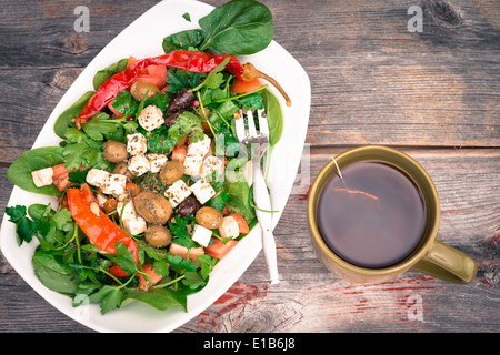 Schüssel mit frischen grünen grünen Baby Spinat und Tomaten-Salat mit einer frisch gebrühten Tasse heißen Tee auf einem rustikalen Holztisch, overhead Stockfoto