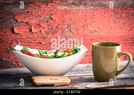 Rustikales Mittagessen eine Schüssel mit Tomaten und Spinat Salat, Tee und ein Stück Brot mit einem Hintergrund von roten Grunge abblätternde Farbe auf ein wo Stockfoto