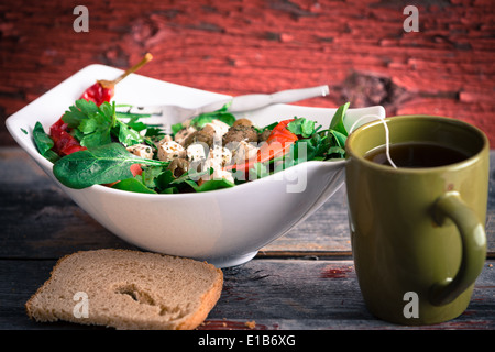 Schüssel mit köstlichen frischen Baby-Spinat, Tomaten und Feta-Salat mit einer Tasse heißem Tee und ein Stück Brot serviert mittags auf ein rus Stockfoto