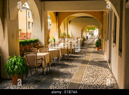 Cafe Tische und Stühle aufgestellt entlang einen bunten überdachten gepflasterten Gehweg in Treviso, Italien. Stockfoto