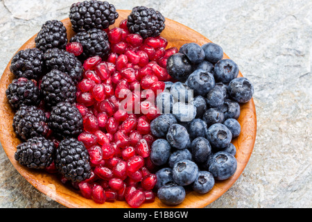 Holzschale frische Heidelbeeren, Brombeeren und Granatapfelkerne in bunten Reihen angeordneten hohen Winkel Blick auf ein altes steinernes Stockfoto