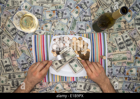 Konzeptbild ein Mann isst Geld durch Extravaganz mit einer Draufsicht auf ihm sitzen am Tisch bedeckt in 100-Dollar- Stockfoto