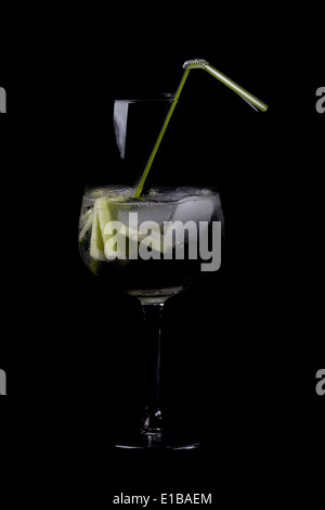 Gin und Tonic serviert in einem Ballonglas mit einem Strohhalm auf schwarz Stockfoto