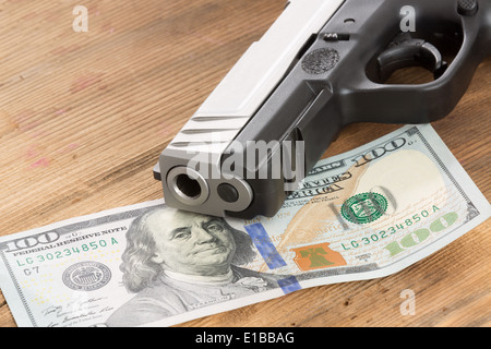 Nahaufnahme von der Mündung einer Pistole mit einem 100 amerikanischen Dollarschein liegen auf einem Holztisch in einem konzeptionellen Bild des Verbrechens, Bestechung Stockfoto
