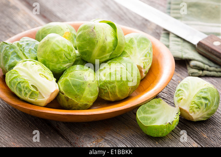 Schüssel mit frischem rohem gereinigt Rosenkohl mit einem halbierten im Vordergrund stehen auf einem alten rustikalen Holzküche t Stockfoto