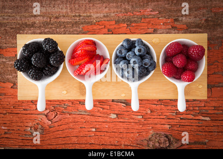 Frische gemischte Beeren auf einer Grunge hölzernen Theke in kleinen Keramik Förmchen einschließlich Brombeeren, Heidelbeeren, Stroh angezeigt Stockfoto