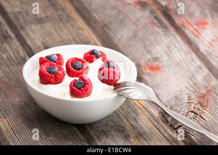 Köstliche frische Himbeeren und Heidelbeeren in einer Schüssel cremig Joghurt für einen gesunden Snack oder Dessert topping serviert mit einem Löffel o Stockfoto