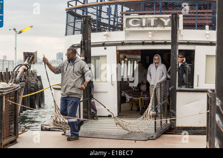 Afrikanische amerikanische männliche Fähre Arbeiter bereitet sich auf die Fähre zu den Docks zu binden, wie Passagiere warten auf die Fähre in Wards Island aussteigen Stockfoto