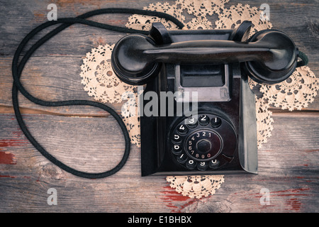 Eine alte schwarze Telefon mit Wählscheibe Detailansicht hohen Winkel auf eine dekorative Criocheted Deckchen mit dem Hörer auf die Gabel Stockfoto