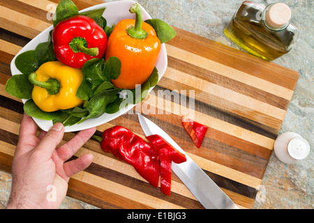 Man bereitet einen gesunden frischen Salat für eine Schale mit bunten süße Paprika in rot, gelb und Orange mit grünen Bab erreichen Stockfoto