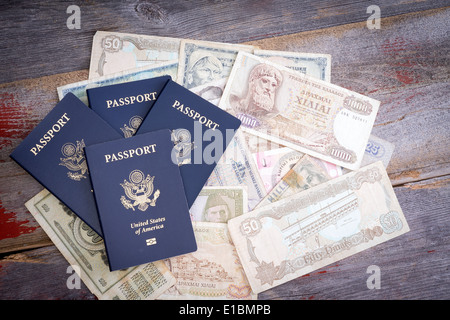 Gruppe von vier amerikanischen Pässe mit ausländischen Banknoten in verschiedenen Währungen auf einem Holztisch, Darstellung, Planung und f liegen Stockfoto