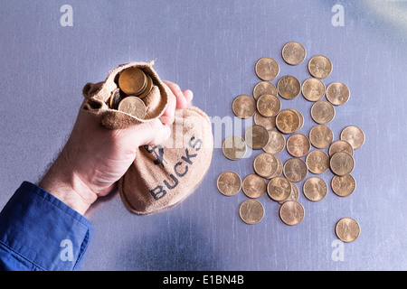 Mann hält ein Geldsack Dollar mit US-Dollar-Münzen liegen verstreut auf dem Tisch unten in ein Konzept der überfüllt Stockfoto