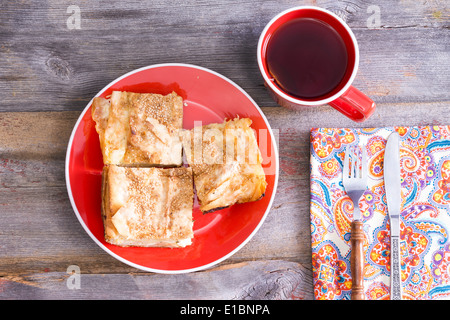 Ansicht von oben drei Quadrate der frische hausgemachte türkische Borek, hergestellt aus Blätterteig Yufka-Teig mit einer Tasse heißer schwarzer Tee serviert Stockfoto