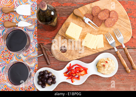 Draufsicht auf herzhafte Snacks auf einem rustikalen Tisch mit zwei Gläser und eine Flasche Rotwein und Havarti Käse, würzig getrocknete Weisswurst Stockfoto