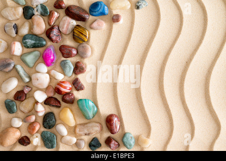 Anordnung der Fersenone Kies und bunte Trommelsteine polierte Edelsteine am goldenen Sandstrand mit einer wellenförmigen Wellenmuster Stockfoto