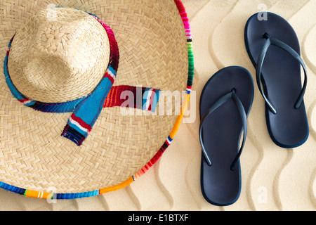 Stroh Sombrero oder Sonnenhut mit einem bunt gestreiften Band und Schlupf-Hose oder Sandalen auf goldenen Sand mit einer wellenförmigen tropischen Strand Stockfoto