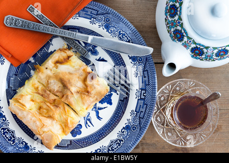 Mit einer Tasse frisch gebrühtem Tee und eine Teekanne serviert leckeres Stück hausgemachten türkischen Börek auf einem Teller mit Besteck Stockfoto