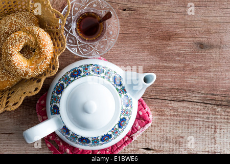 Kännchen Tee mit frischem türkischen Sesam Bagels in einem Brotkorb serviert mit einer heißen Tasse türkischen Tee auf einem rustikalen Holztisch mit Stockfoto