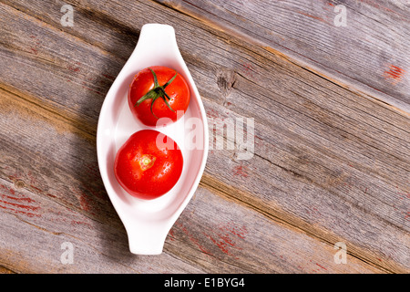 Zwei saftige Reife rote Tomaten in eine kleine weiße Keramik Schale so angeordnet, dass die grüne Stiel nach oben auf einen zeigt und auf th entfernt Stockfoto