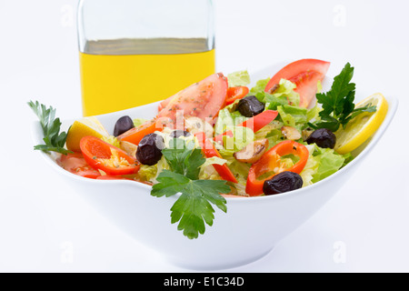 Frischer mediterraner Salat mit Oliven, Tomaten, Petersilie, Zitrone, Paprika, Salat mit Olivenöl extra vergine im Hintergrund Stockfoto
