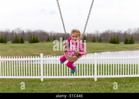 Schöne begeistert kleine Mädchen auf Gartenschaukel schreien vor Freude, lachen, als sie hoch in die Luft gegen ländliche Backgroud fliegt Stockfoto