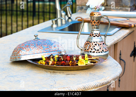 Gegrillte türkische Schaschliks mit erfahrenen Fleisch und Gemüse, serviert auf einer gewölbten Kupferplatte mit einem passenden eleganten Krug Stockfoto