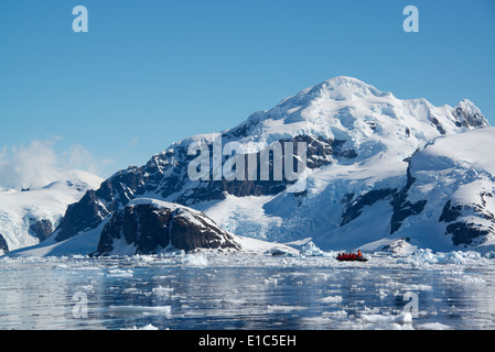 Ein kleines Boot schwimmt auf dem Ozean unter den Eisschollen vor der Küste einer Insel in der Antarktis. Stockfoto