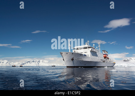 Eine Antarktis Kreuzfahrt Schiff mit aufblasbaren Schlauchboote auf dem ruhigen Wasser unter den Eisschollen und bergige Landschaft. Stockfoto