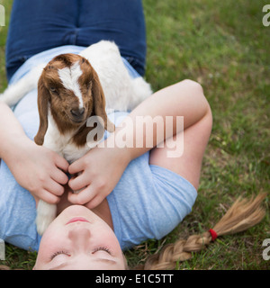 Ein Mädchen kuscheln eine Baby-Ziege liegend auf der Brust. Stockfoto