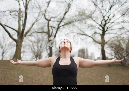 Eine junge Frau im Central Park, in einem schwarzen Anzug und Leggings, Yoga zu tun. Stockfoto