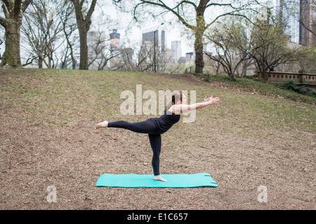 Eine junge Frau im Central Park, in einem schwarzen Anzug und Leggings, Yoga zu tun. Stockfoto