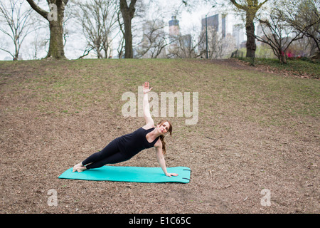 Eine junge Frau im Central Park, in einem schwarzen Anzug und Leggings, Yoga zu tun. Stockfoto