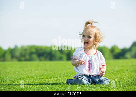 Lächelndes kleines Mädchen sitzt auf einem frischen grünen Rasen in einem Feld, Spaß Stockfoto