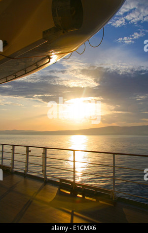 Offenes Deck eines Kreuzfahrtschiffes bei Sonnenuntergang an der Küste in der Ferne. Sonne ist Einstellung & scheint auf dem Ozean, Karibik. Stockfoto