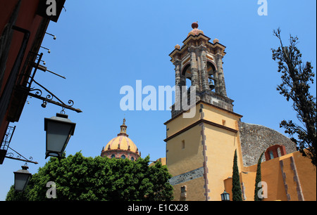 Gelbe Kirche mit Glockenturm und Kuppel gesehen von der Straße mit einer Lampe overhead, San Miguel de Allende, Guanajuato, Mexic Stockfoto