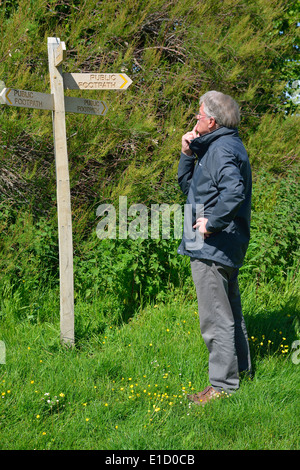 Mann, eine Richtungswahl stand neben einem hölzernen öffentlichen foothpath Wegweiser (finger Post) bei Snow Hill, West Wittering, West Sussex, Großbritannien Stockfoto