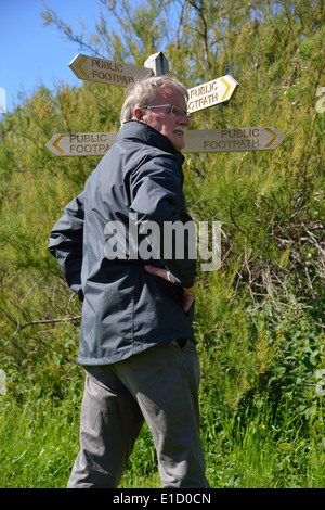 Mann, eine Richtungswahl stand neben einem hölzernen öffentlichen foothpath Wegweiser (finger Post) bei Snow Hill, West Wittering, West Sussex, Großbritannien Stockfoto