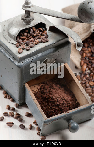alte Kaffeemühle mit Sackleinen und Kaffeebohnen auf Holztisch Stockfoto