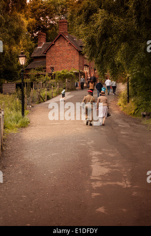 Mann und Frau, die Hand in Hand gekleidet in 40er Jahren historischen Kostümen zu Fuß entlang einer Landstrasse, durch eine Straße Gas Licht beleuchtet. U.K Stockfoto