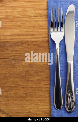 Messer und Gabel auf Serviette auf Holzbrett Stockfoto