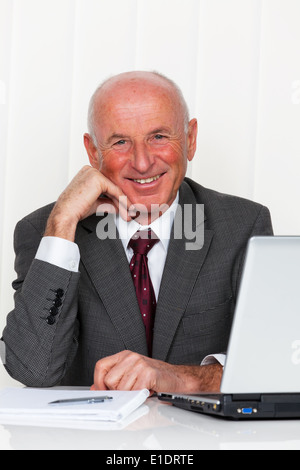 Ein erfolgreicher älteren Geschäftsmann sitzt in seinem Büro mit einem Laptop. Stockfoto