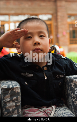 Kind mit schweren Ausdruck tut den militärischen Gruß in einem Waisenhaus in Peking Stockfoto