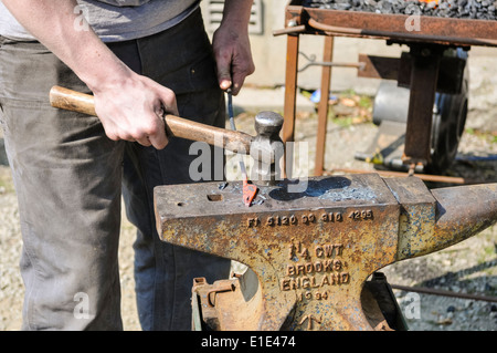 Schmied benutzt einen Hammer und Amboss, eine Eisenstange zu gestalten Stockfoto