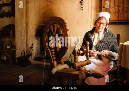 Eine Frau im 19. Jahrhundert Kleidung Spins Wolle mit einem traditionellen Spinnrad in Ulster American Folk Park, Norther Stockfoto