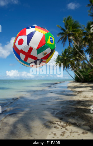 Internationale Fahne Ball Fußball fliegen in den Himmel über tropischen brasilianischen Strand Palmen Schatten in Nordeste Bahia Brasilien Stockfoto