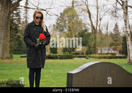 Junge Frau am Grab eines verstorbenen Familienmitglieds stehen. Frau am Friedhof trauernde Blumen halten. Stockfoto