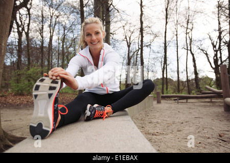 Glücklich und Fit Frau dehnen ihre Beine vor Training in der Natur. Schöne kaukasischen Athlet im Park trainieren. Stockfoto